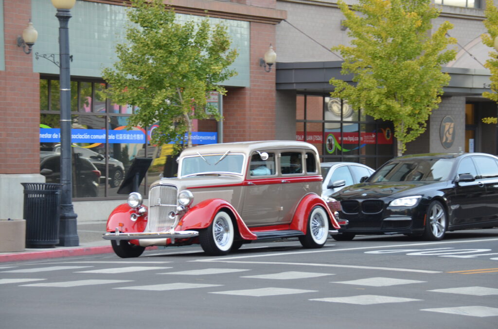 Photo shows a classic 1940s car driving on a street, the driver is slightly visible through the window